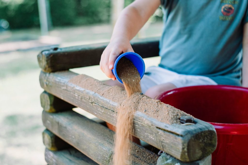 toddler pouring sand in brown wooden fence